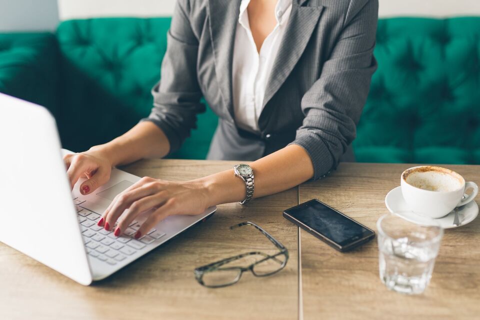 Hands typing on a laptop beside a notebook